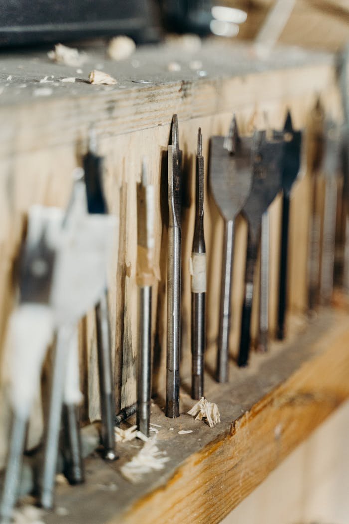 Close-up of various drill bits on a wooden shelf in a workshop setting.